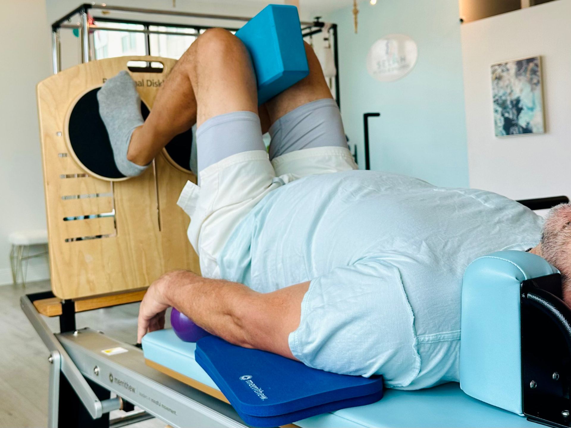 A client lying on the reformer carriage with a prop under the knees during a private session