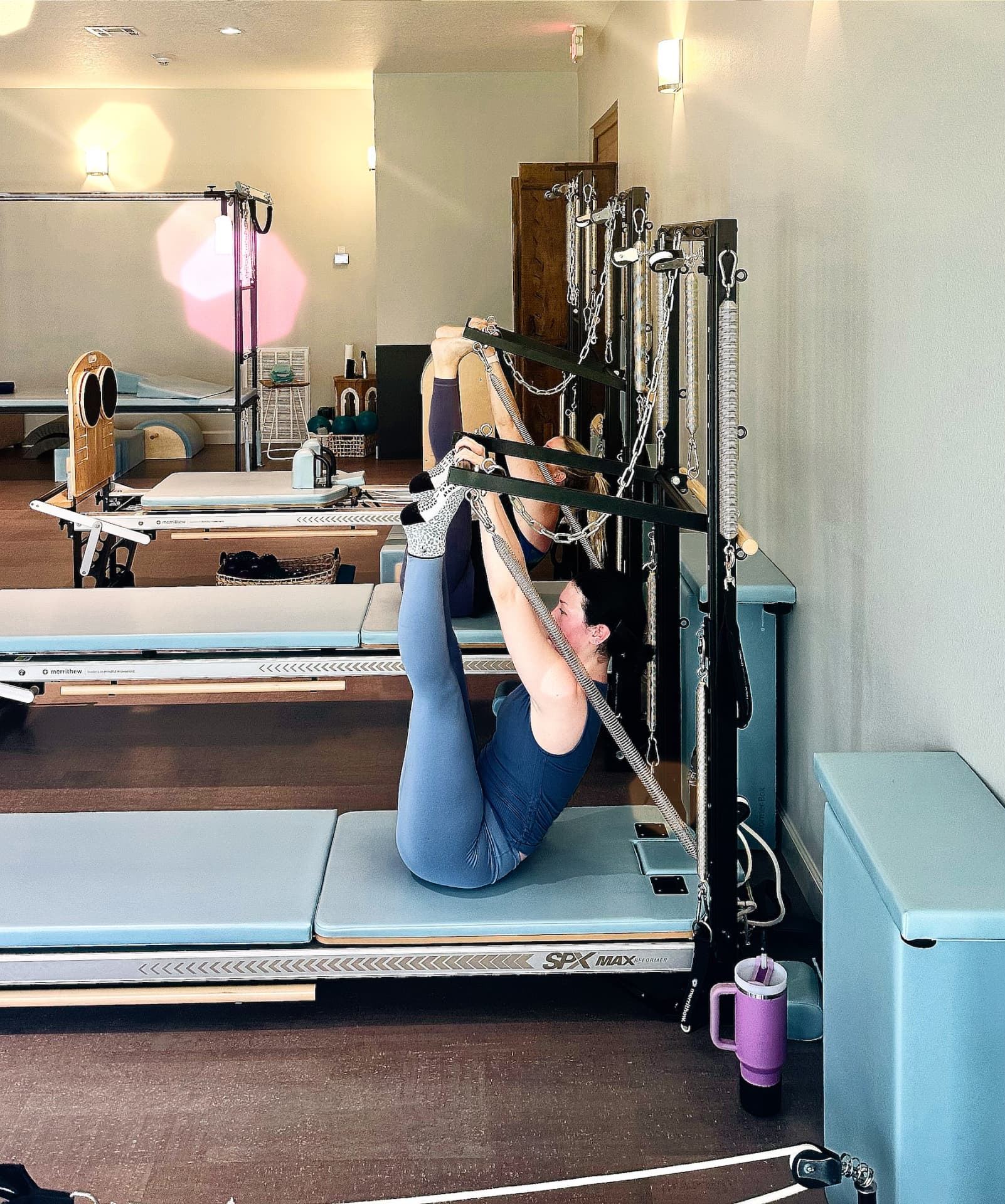 A client kneeling at the tower, pulling on spring-loaded straps to open through the chest